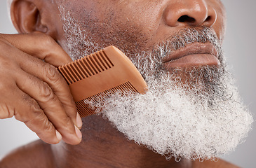 Image showing Senior man, hands and beard with comb in grooming, beauty or skincare hygiene against a studio background. Closeup of African elderly male face combing or brushing facial hair for clean wellness