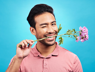 Image showing Teeth, flower and wink with portrait of man in studio for celebration, gift and romance. Funny, goofy and present with male isolated on blue background for flirting, smile and valentines day mockup