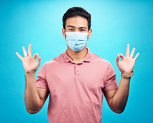 Image showing Man in face mask, portrait and covid with okay hand gesture, safety from virus and bacteria isolated on blue background. Disease, corona and male person with emoji and health compliance in studio