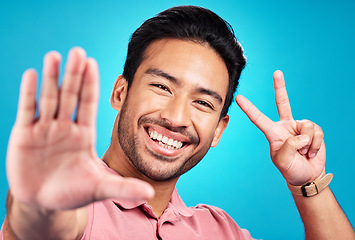 Image showing Happy asian man, portrait and peace sign for selfie, profile picture, or social media against a blue studio background. Male influencer or vlogger with smile showing peaceful emoji for photo or vlog