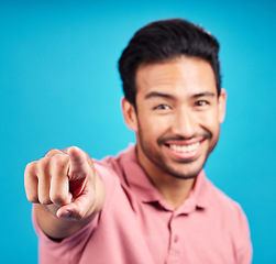 Image showing Pointing, focus and portrait of man in studio for motivation, choice and decision. Happy, smile and yes with male and hand gesture isolated on blue background for hey you, offer and emoji mockup