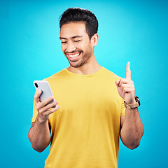 Image showing Number one, phone and man isolated on blue background for online question, idea or decision on mobile app. Happy asian person or user with smartphone, internet or website and pointing up in studio