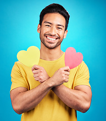 Image showing Portrait, smile and man with heart cutout in studio isolated on a blue background. Love, happiness and Asian person with symbol, sign or emoji for affection, care and romance, empathy and valentines.