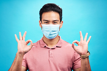 Image showing Man in face mask, portrait and corona with okay hand sign, safety from virus and bacteria isolated on blue background. Disease, covid and male person with emoji and health compliance in studio