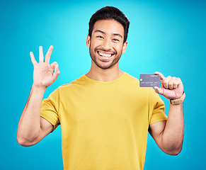 Image showing Credit card, okay and portrait of man isolated on blue background for shopping, e commerce and payment loan. Happy asian person, excited for banking solution, financial savings and ok emoji in studio