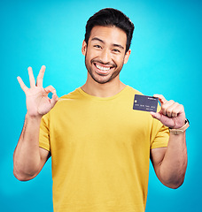 Image showing Ok, credit card and man in portrait isolated on blue background for shopping, e commerce and payment loan. Happy asian person, excited for banking solution, financial savings and okay emoji in studio