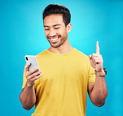 Image showing Asian man, phone and man pointing up with idea, solution or question against a blue studio background. Happy person or user on mobile smartphone, internet or website and point for solving on mockup