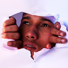 Image showing Face, wall and a man looking through a hole to discover, explore or search while on an adventure. Head, eyes and thinking with a handsome young male closeup in studio to look out from a tear or gap