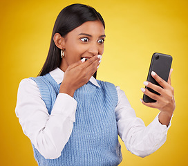 Image showing Wow, surprise and woman with phone in studio space reading text or email on yellow background. Technology, communication and good news, happy Indian girl with social media gossip or online content.