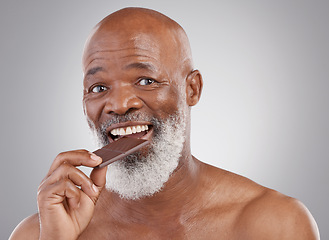 Image showing Black man, portrait and eating chocolate sweets isolated on a studio background for a treat. Happy, snack smile and an elderly African model biting into a sweet candy bar for happiness and sugar