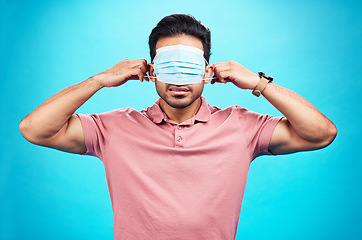 Image showing Face mask, cover eyes and a man with blindfold isolated on a blue background in a studio. Struggling, virus and a person with covid wearing a tool to protect from sickness, hiding facial sight