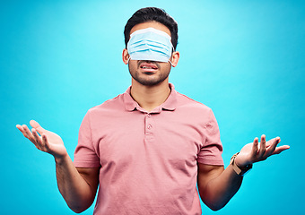 Image showing Face mask, covid and man in blindfold shrugging in studio for doubt, medical misinformation or conspiracy theory. Confusion, virus or person with ppe isolated on blue background for pandemic question