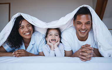 Image showing Happy, love and portrait of a family on a bed in their bedroom relaxing and bonding together. Happiness, smile and girl child laying with her mother and father with a blanket in their modern home.