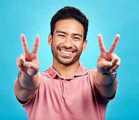 Image showing Portrait, peace sign and Asian man with a smile, support and confident on a blue studio background. Face, male person or model with v gesture, emoji and symbol with happiness, hands and peaceful icon