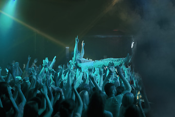 Image showing Crowd surf, blue light and people at concert or at music festival, lights and energy at live event. Dance, fun and group of excited fans in arena at rock show performance, group carrying fan on hands