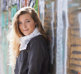 Image showing Portrait, urban fashion and woman at wall with smile, graffiti and standing at outdoor street art. Happiness, youth and happy face of gen z model in city with streetwear, winter style and sunshine.