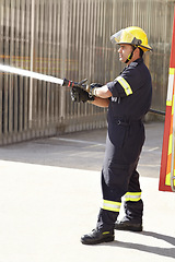 Image showing Male firefighter, spray water and emergency worker with helmet, uniform and brave to stop inferno. Fireman, fire hose and fearless on mission to rescue, health and safety service at job outdoor