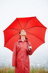 Image showing Rain, happy and red umbrella with woman in nature for winter, storm and carefree. Happiness, weather and cold with female wearing raincoat in outdoor for waterproof, cloudy and protection