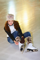 Image showing Portrait, ice skating and woman tie shoes on rink to start fitness, exercise and workout at night. Skater, happiness and female person tying skates for winter training, getting ready and top view.