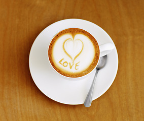 Image showing Coffee cup, cappuccino and heart in foam on a table with no people in a restaurant and diner. Cafe drink, love writing and foamy beverage art with milk in a cafe with a closeup of mug and spoon