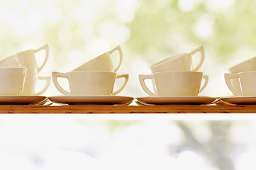 Image showing Collection, tea or coffee mug closeup and porcelain cup with plate on window shelf with background mockup. White, ceramic and breakfast catering service set for party and cafe, hotel or restaurant