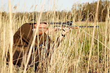 Image showing Nature, hunter and man with a rifle while in camouflage shooting in outdoor field. Grass, wildlife and male sniper hunting animals with shotgun weapon hiding in plants to shoot target in countryside.