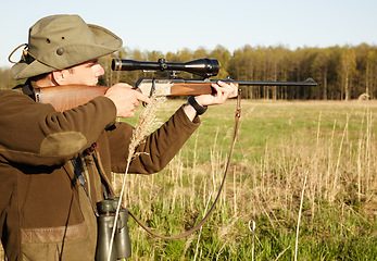 Image showing Hunting, rifle and target with a ranger man aiming a weapon on a field outdoor in nature for sport. Gun, scope and shooting with a male game hunter holding a sniper outside in a grass environment