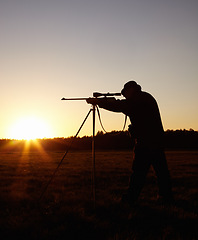 Image showing Hunting at sunset, man with rifle stand in nature to hunt game for sport on safari adventure. Sky, silhouette and hunter with gun, focus on target and evening setting sun for shooting hobby in bush.