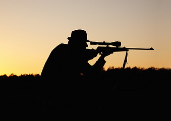 Image showing Hunting, sunset, man with gun and focus on target in nature to hunt game for sport on safari adventure. Sky, silhouette and hunter with rifle in bush, setting sun and shooting hobby on summer evening