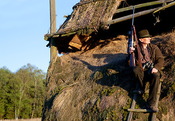 Image showing Hunter, game shooting and man on a safari gun at outlook post for animal and wild hunting. Male person, poacher and hunter waiting for wildlife sports outdoor for scope watching at sunrise as a hobby