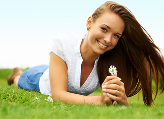 Image showing Portrait, smile and woman with daisy on grass, lying down on field and enjoying spring on vacation outdoor. Happy, flower plant and beauty of female person relaxing, smiling and having fun in nature.