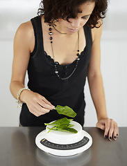 Image showing Woman, scale and spinach in kitchen for food, diet or eating disorder with leaves for meal plan. Girl, mental health and vegetable leaf to lose weight with anorexia, bulimia or starving in house