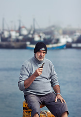 Image showing Fisherman, mature man portrait and smoking pipe by the sea water at a port for fishing. Old man, ocean and senior dock worker sitting by boats outdoor with tobacco smoke at a harbor for work