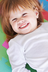 Image showing Young girl, laughing and happiness portrait of a baby on a home playpen ground with a smile. Ginger infant, kid laugh and happy in a house with joy, youth and positivity from childhood looking up