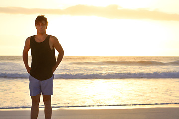 Image showing Portrait, mockup and a man on the beach at sunset standing on sand by the sea at the coast outdoor. Nature, water and travel with a handsome young male tourist at the ocean during holiday or vacation