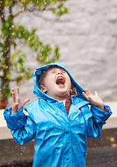 Image showing Wet weather, raincoat and a girl playing in the rain outdoor alone, having fun during the cold season. Kids, winter or freedom with an adorable little female child standing arms outstretched outside