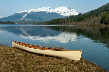 Image showing Canoe lying by the water and mountains reflected in the water