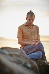 Image showing Calm and collected just as nature intended. Shot of a peaceful man sitting on a rock during his yoga routine at the beach.