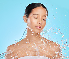 Image showing Skincare, water and face of woman on blue background for wellness, healthy skin and cleaning in studio. Bathroom, shower and female person with liquid splash for facial grooming, washing and beauty