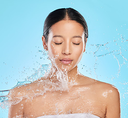 Image showing Skincare, water splash and face of woman on blue background for wellness, healthy skin or cleaning. Bathroom, shower and eyes closed of female person for facial grooming, washing and beauty in studio