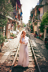 Image showing Every town I visit becomes part of me. Shot of a young woman walking on train tracks through the streets of Vietnam.