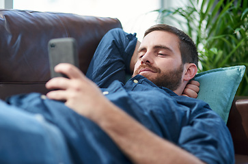 Image showing Recharge and bounce back better than ever. Shot of a young man using a smartphone while relaxing on a sofa.