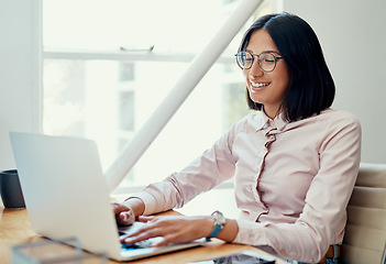 Image showing Working through my day with a smile. Cropped shot of an attractive young businesswoman sitting alone and using her laptop in the office.