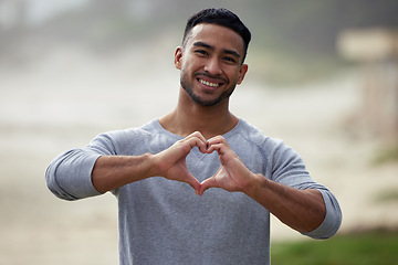 Image showing Portrait of happy man, heart and hand outdoor for care, kindness and emoji for charity, mental health and joy. Young guy, self love and finger shape of hands for thank you, trust and hope with smile