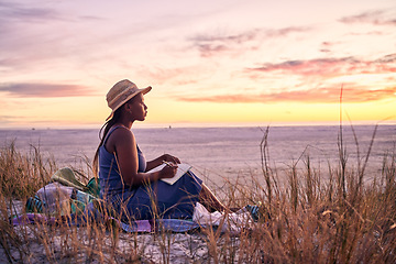 Image showing Black woman, relax and book on beach in sunset with diary or journal for vacation in nature outdoors. African female person relaxing on ocean coast with notebook in morning sunrise and holiday travel