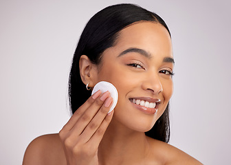 Image showing Happy woman, cotton pad and cleaning face in skincare for makeup removal against a grey studio background. Portrait of female person wiping product, cosmetics or remove with swab for facial treatment