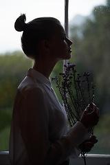 Image showing Dawn beauty. A silhouette of a beautiful young woman holding some flowers and enjoying their scent.