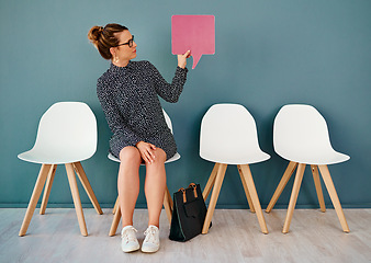 Image showing What do you mean by that. Studio shot of an attractive young businesswoman holding up a speech bubble while siting in line against a grey background.