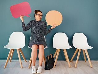 Image showing I dont know whos right either. Studio portrait of an attractive young businesswoman holding up speech bubbles while sitting in line against a grey background.