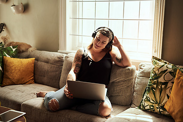 Image showing Sundays are for marathon movie streaming sessions. Shot of a young woman using a laptop and headphones on the sofa at home.